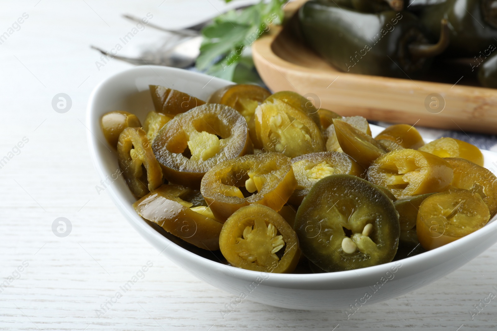 Photo of Bowl with slices of pickled green jalapeno peppers on white wooden table, closeup