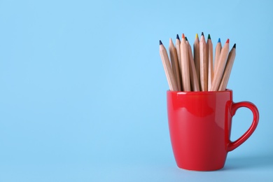 Photo of Colorful pencils in cup on light blue background. Space for text