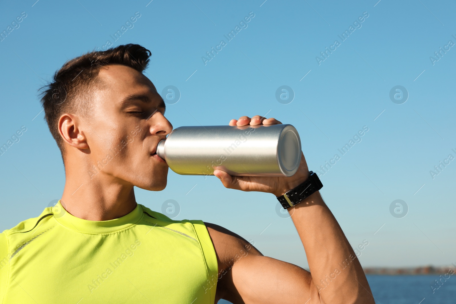 Photo of Young sporty man drinking from water bottle outdoors on sunny day