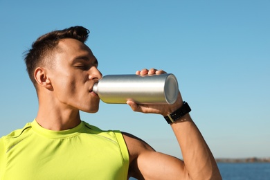 Photo of Young sporty man drinking from water bottle outdoors on sunny day