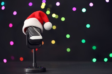 Retro microphone with Santa hat on table against blurred lights, space for text. Christmas music