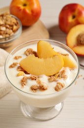 Photo of Tasty peach yogurt with granola and pieces of fruit in dessert bowl on white wooden table
