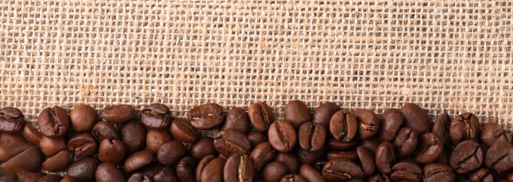 Many coffee beans on burlap fabric, top view. Space for text