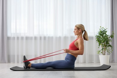 Photo of Athletic woman doing exercise with fitness elastic band on mat at home