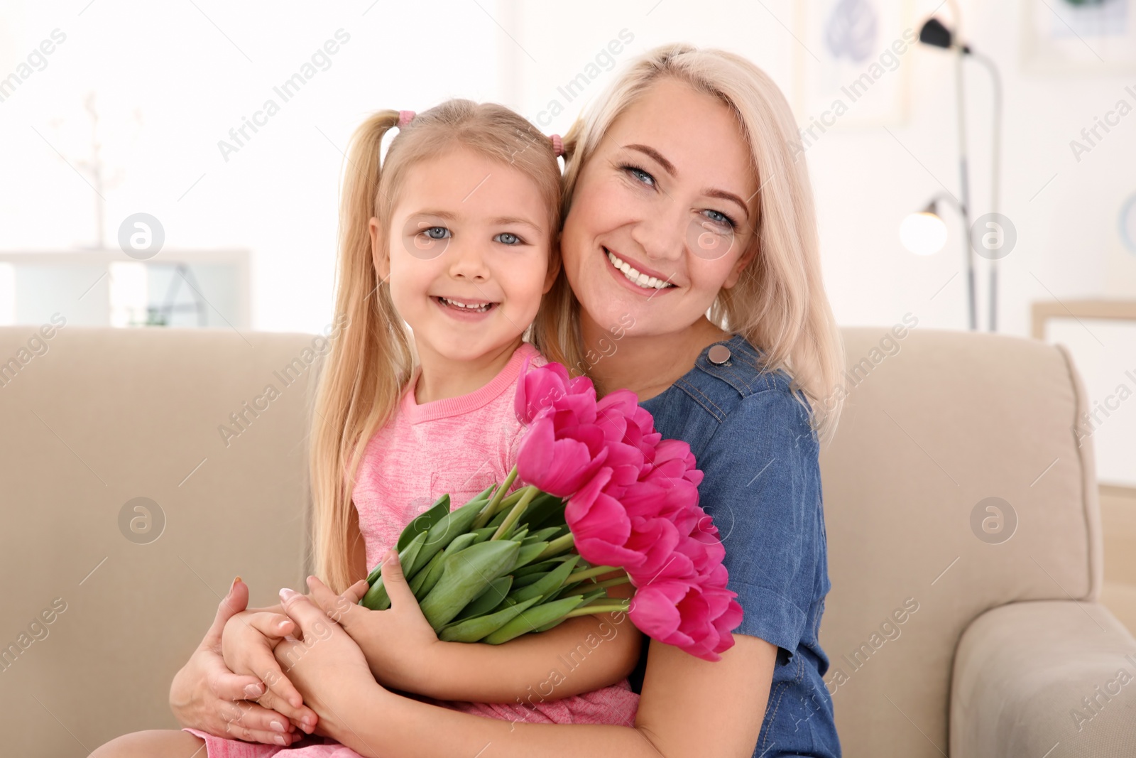 Photo of Happy little girl and her grandmother with tulip bouquet at home