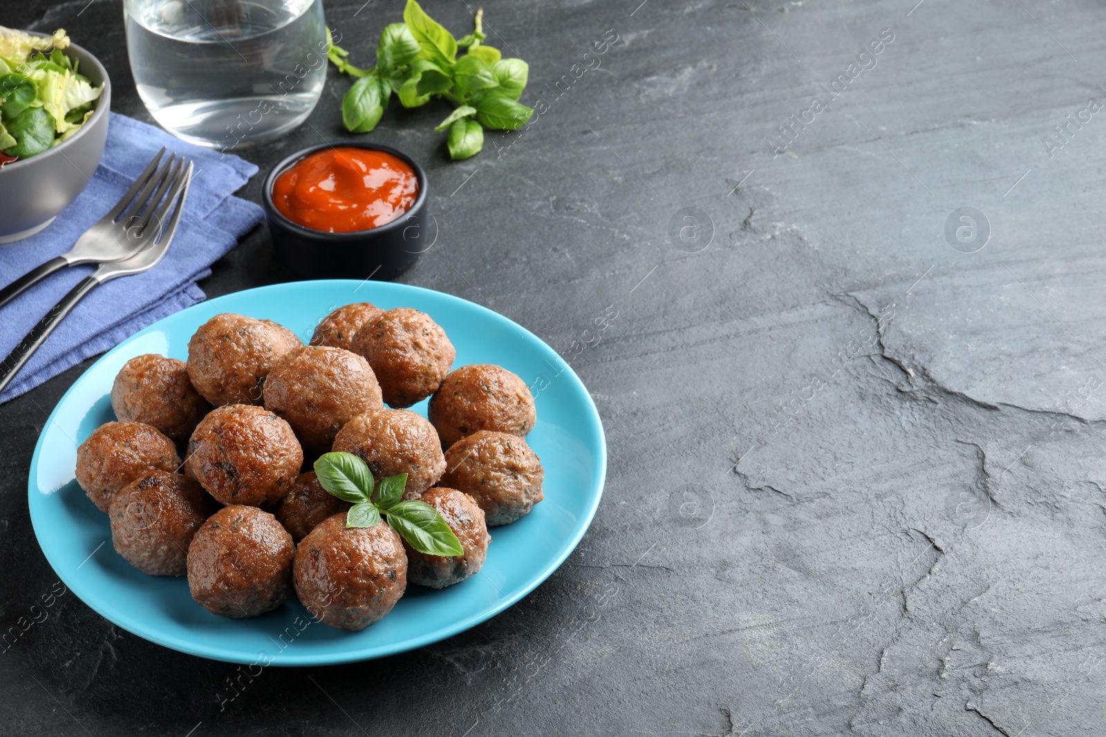 Photo of Tasty cooked meatballs with basil served on black table. Space for text