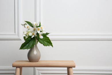 Photo of Beautiful bouquet with fresh jasmine flowers in vase on wooden table indoors, space for text