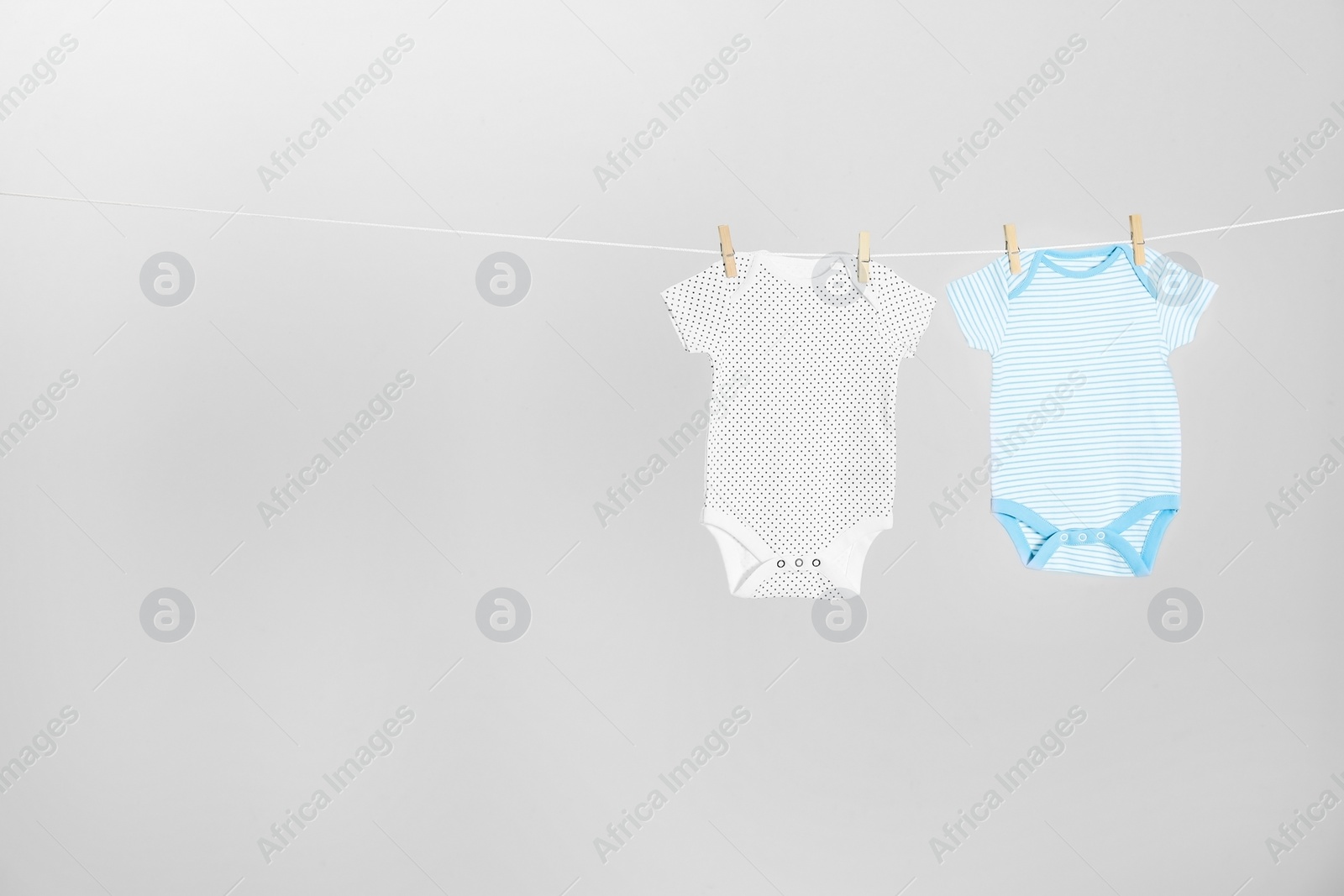 Photo of Different baby onesies hanging on clothes line against light grey background, space for text. Laundry day