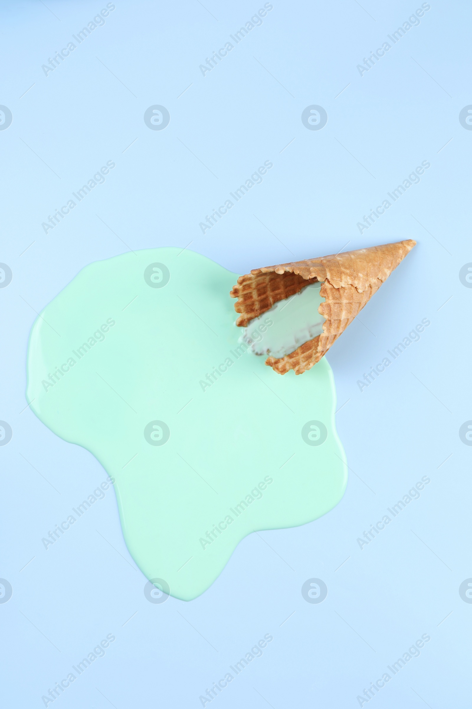 Photo of Melted ice cream and wafer cone on light blue background, top view