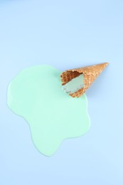 Photo of Melted ice cream and wafer cone on light blue background, top view