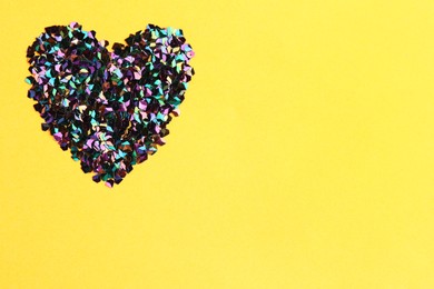 Photo of Heart made with shiny glitter on yellow background, flat lay. Space for text