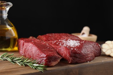 Photo of Fresh raw beef cuts with oil and spices on wooden board, closeup