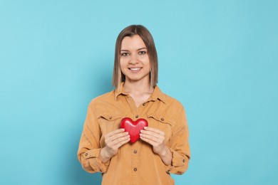 Young woman holding red heart on turquoise background. Volunteer concept