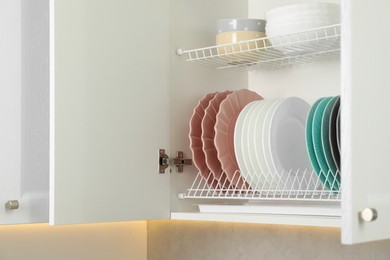 Photo of Clean plates and bowls on shelves in cabinet indoors