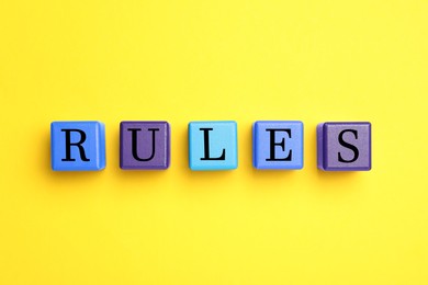 Photo of Word Rules made of wooden cubes with letters on yellow background, flat lay