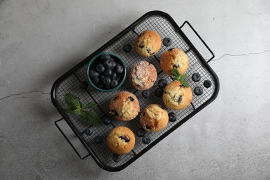 Photo of Delicious muffins with powdered sugar, blueberries and mint on light grey table, top view