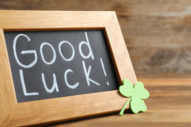 Photo of Blackboard with phrase GOOD LUCK and clover leaf on wooden table, closeup