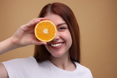 Smiling woman covering eye with half of orange on beige background