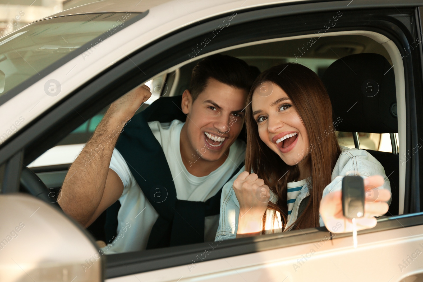 Photo of Happy couple with car key sitting in modern auto at dealership