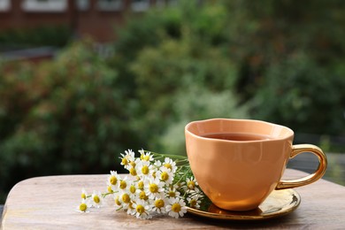 Cup of delicious chamomile tea and fresh flowers outdoors. Space for text