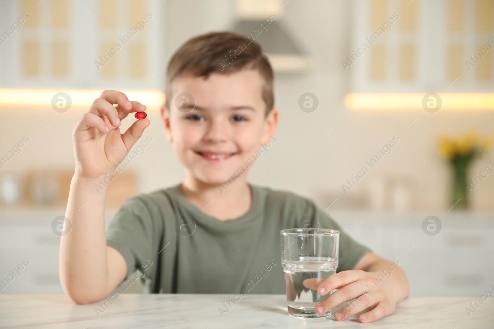 Photo of Little boy with glass of water and vitamin capsule in kitchen, focus on hands