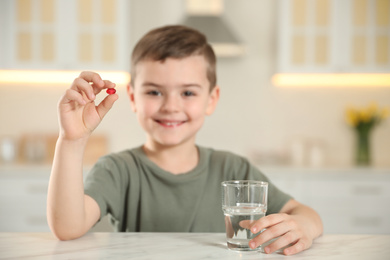 Little boy with glass of water and vitamin capsule in kitchen, focus on hands