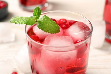 Tasty cranberry cocktail with ice cubes in glass on white table, closeup