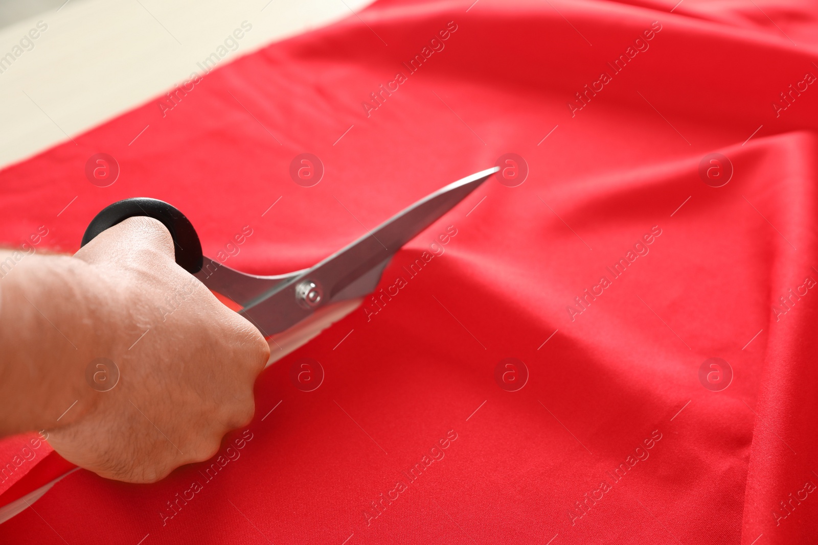 Photo of Professional tailor cutting red fabric with scissors in workshop, closeup
