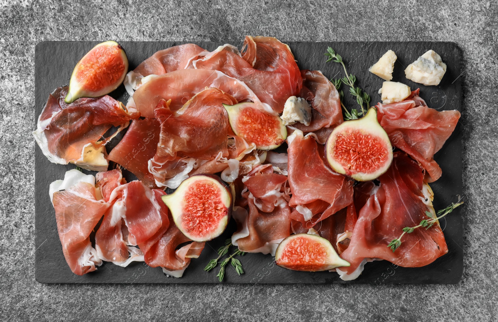 Photo of Delicious ripe figs and prosciutto served on grey table, flat lay