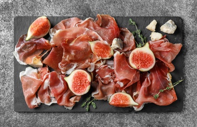 Delicious ripe figs and prosciutto served on grey table, flat lay