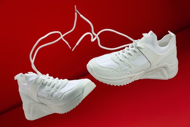 Photo of Pair of stylish white sneakers in air against red background