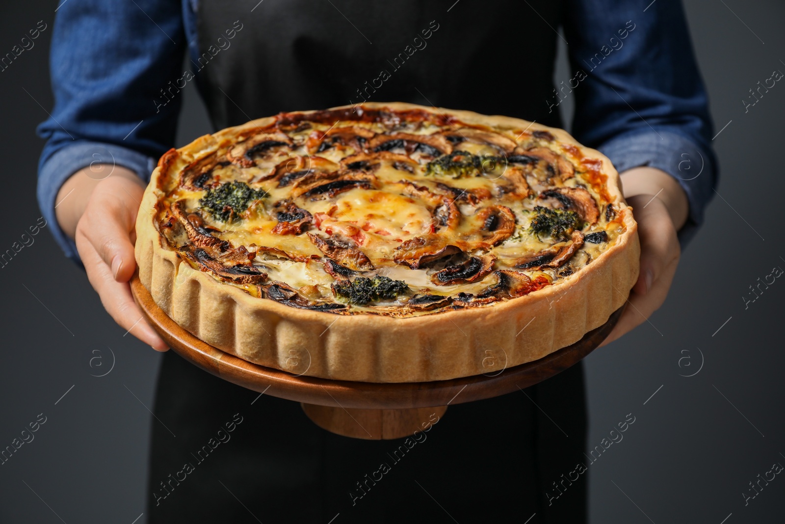 Photo of Woman holding delicious quiche with mushrooms on dark grey background, closeup
