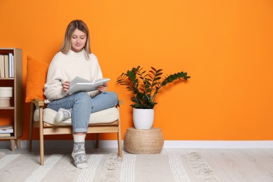 Young woman reading book in armchair at home, space for text. Interior design