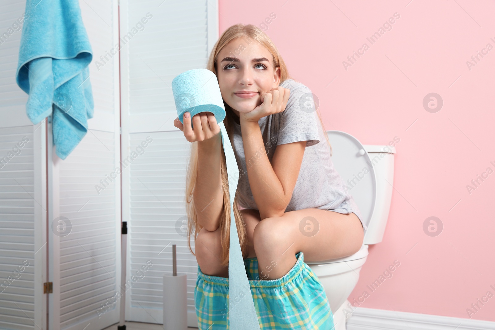 Photo of Woman with paper roll sitting on toilet bowl in bathroom