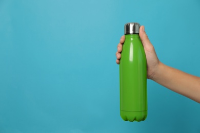 Woman holding modern green thermos on light blue background, closeup. Space for text