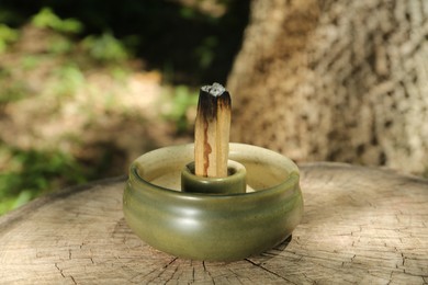 Smoldering palo santo stick in holder on wooden stump outdoors