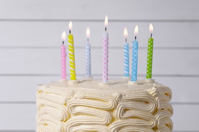 Photo of Delicious cake with cream and burning candles near white wall, closeup
