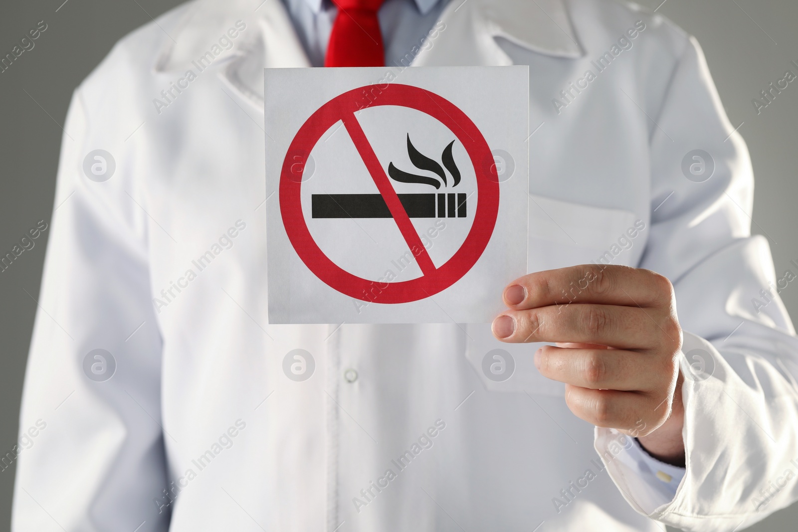 Photo of Doctor holding card with no smoking sign on gray background, closeup