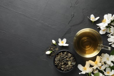 Photo of Glass cup of jasmine tea and fresh flowers on black table, flat lay. Space for text