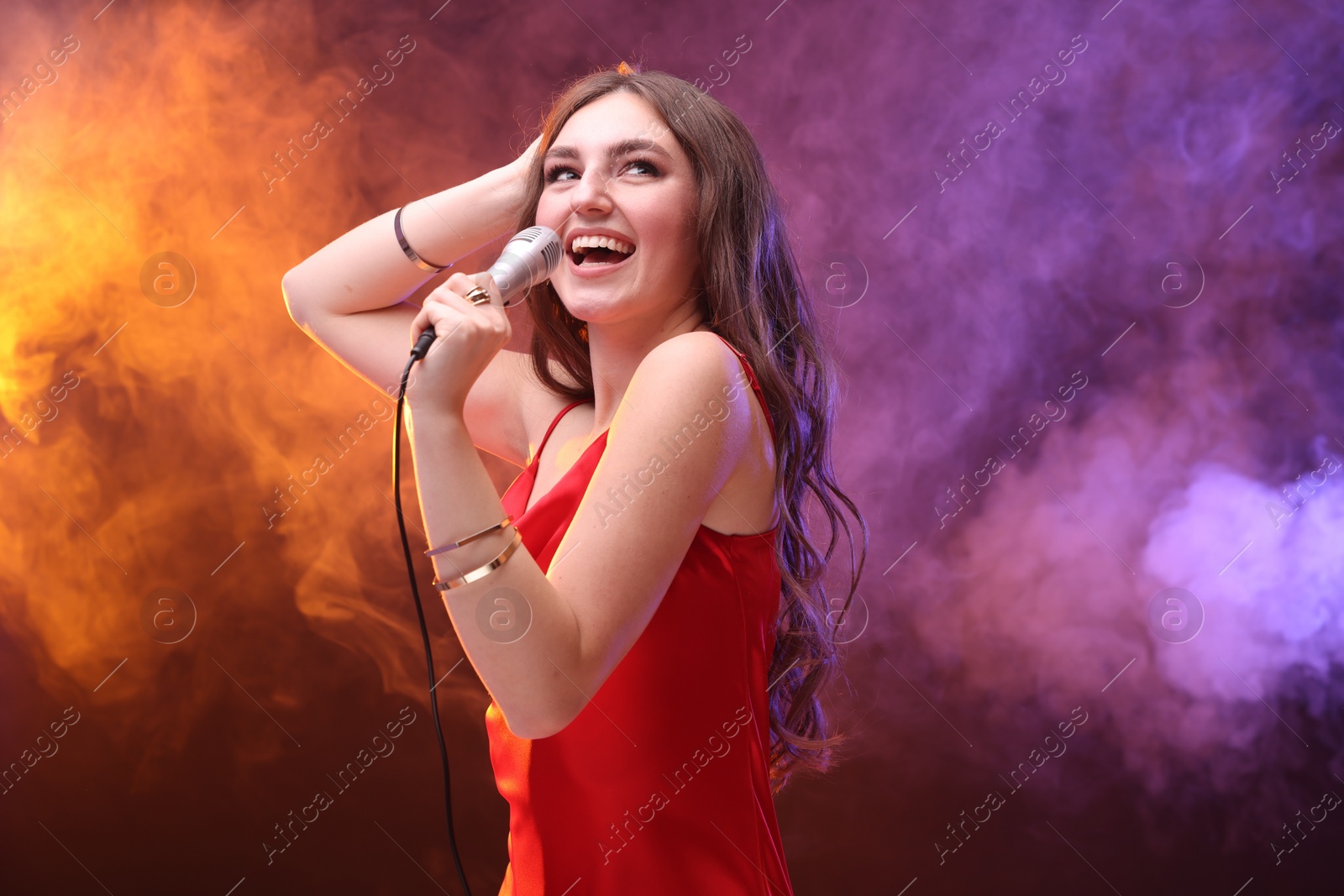 Photo of Emotional woman with microphone singing in color lights. Space for text