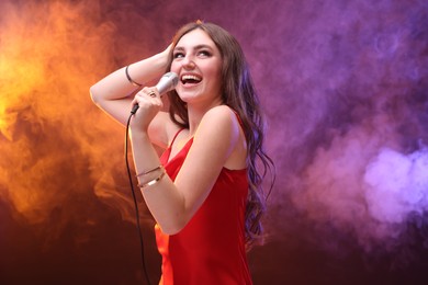 Emotional woman with microphone singing in color lights. Space for text