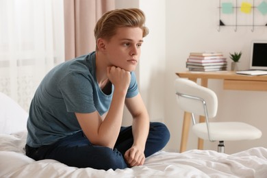Photo of Upset teenage boy sitting on bed at home
