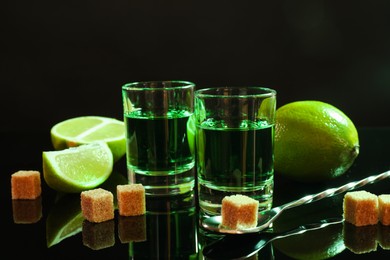 Photo of Absinthe in shot glasses, brown sugar, lime and spoon on mirror table. Alcoholic drink