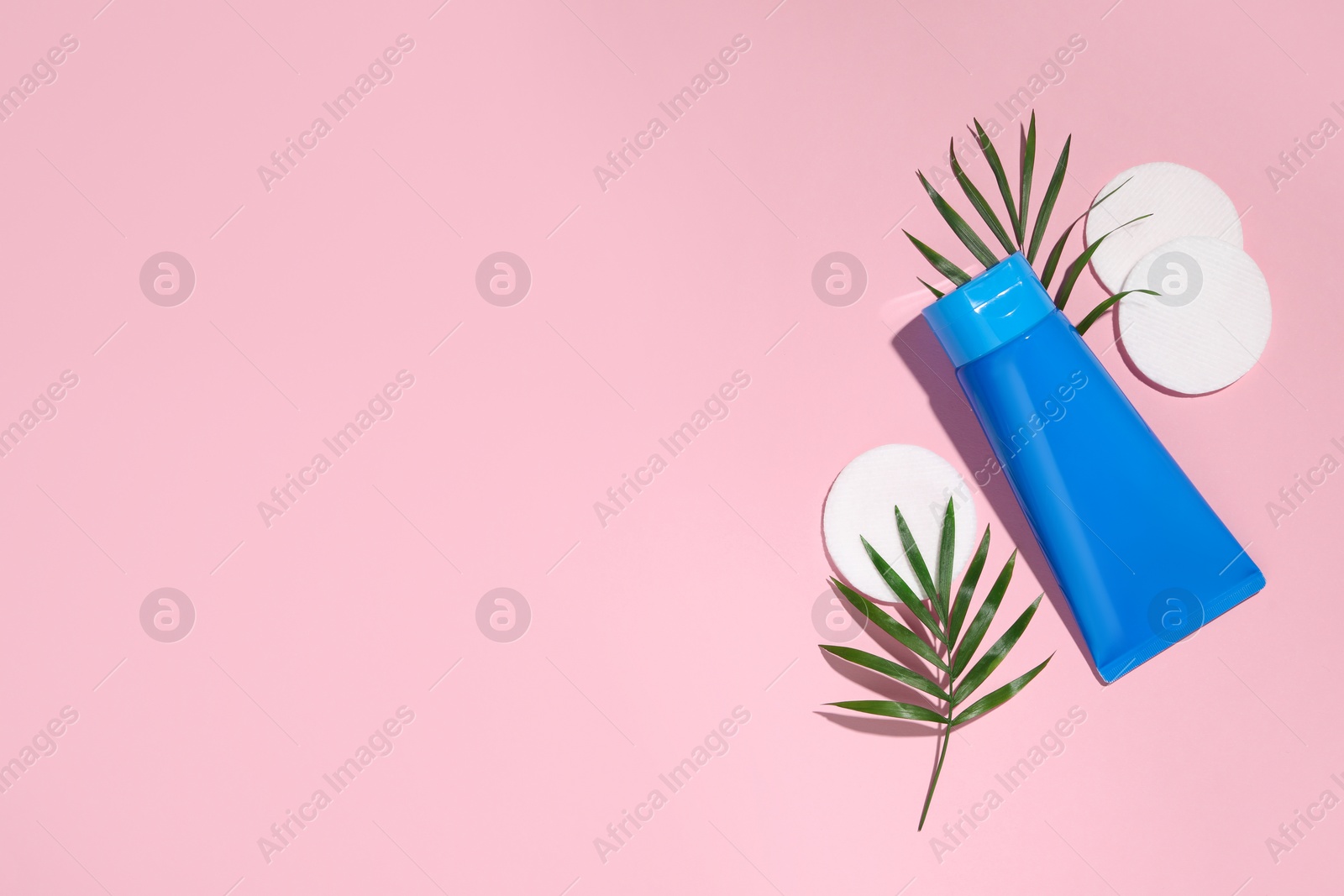 Photo of Tube of face cleansing product, leaves and cotton pads on pink background, flat lay. Space for text