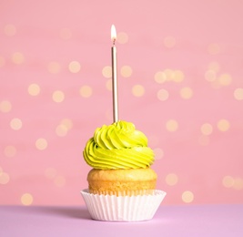 Photo of Birthday cupcake with candle on table against festive lights