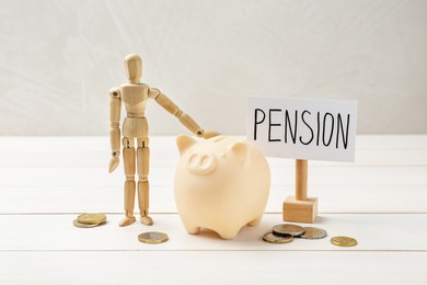 Pension savings. Piggy bank, coins and mannequin on white wooden table