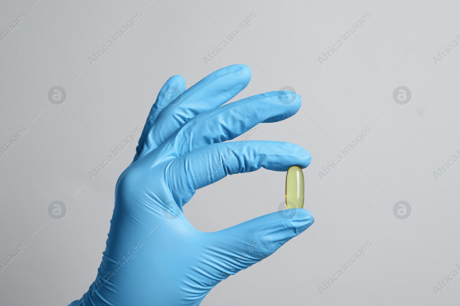 Photo of Doctor holding pill on grey background, closeup