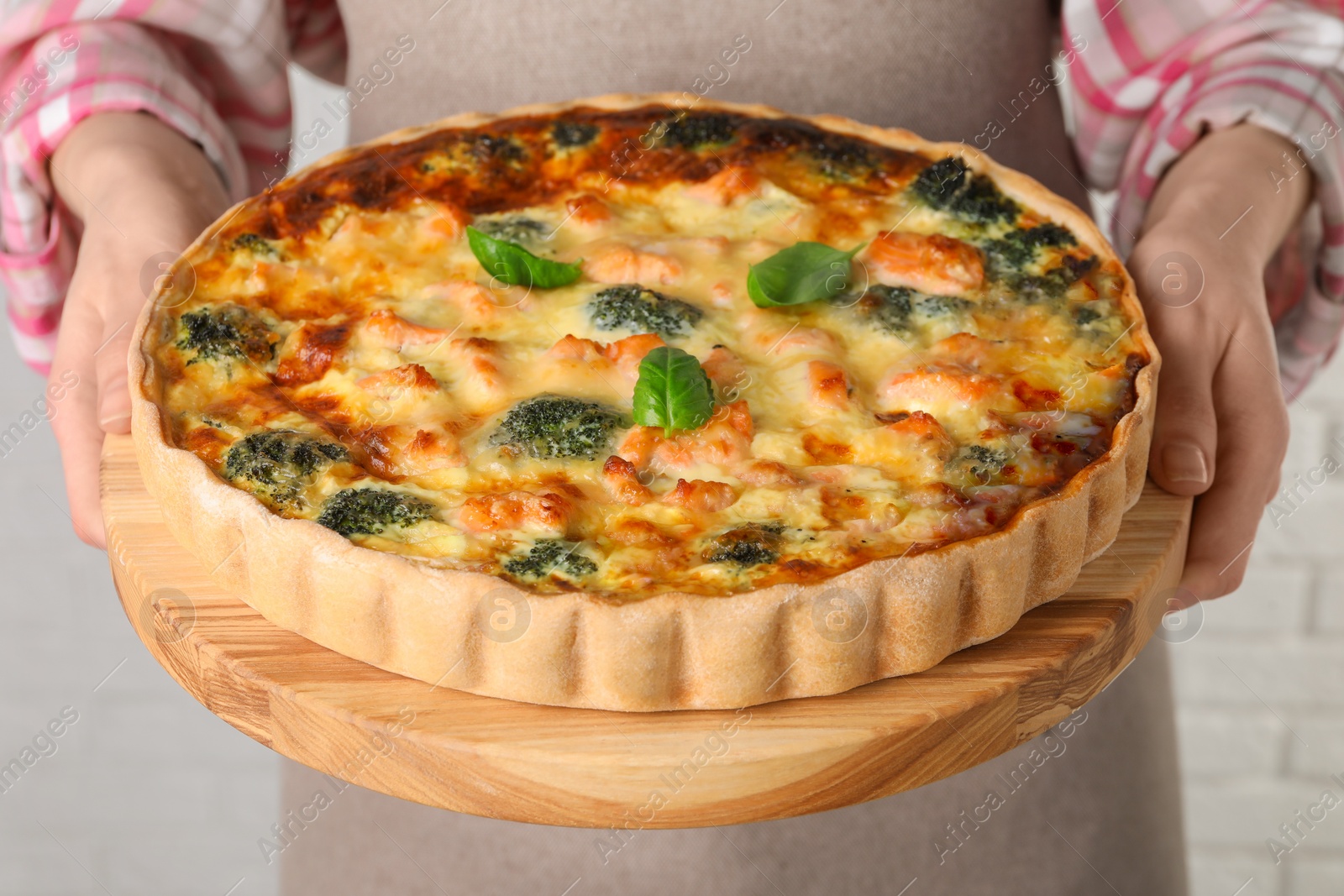 Photo of Woman holding delicious homemade quiche with salmon and broccoli on light background, closeup