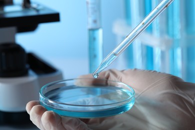 Photo of Scientist dripping liquid from pipette into petri dish in laboratory, closeup