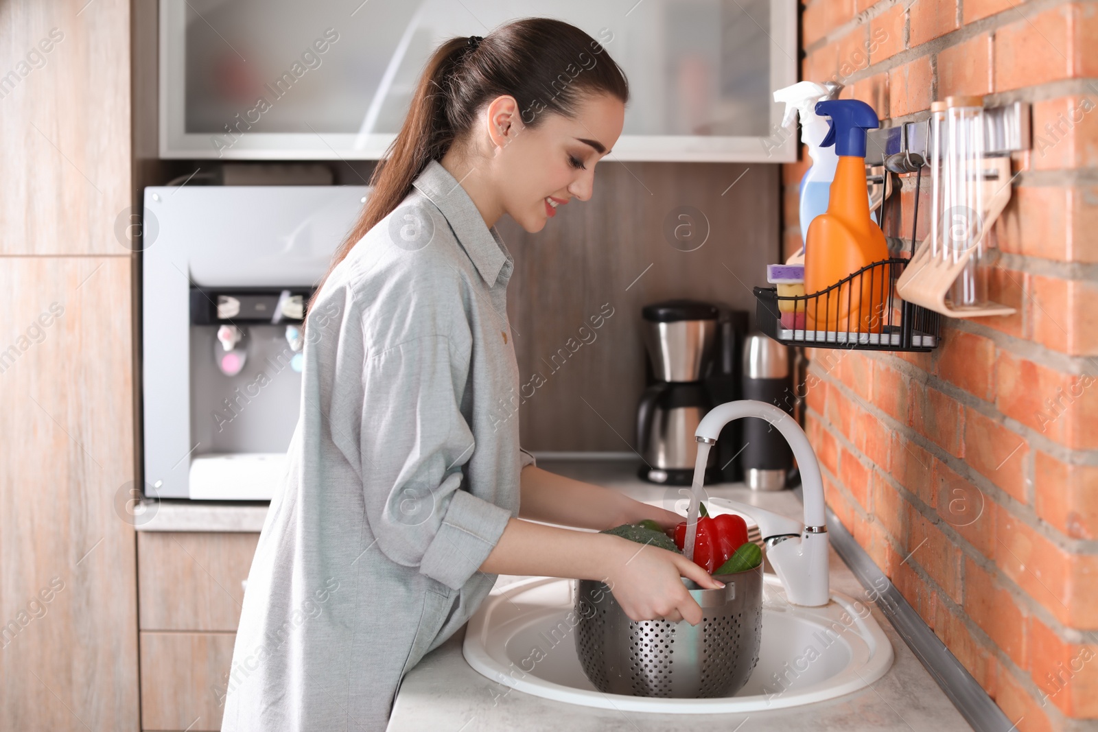 Photo of Young woman washing vegetables in kitchen